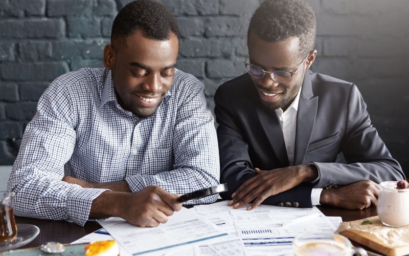 happy african american office workers dressed formal clothing having cheerful looks studying amalyzing legal documents table using magnifying glass while getting papers ready meeting